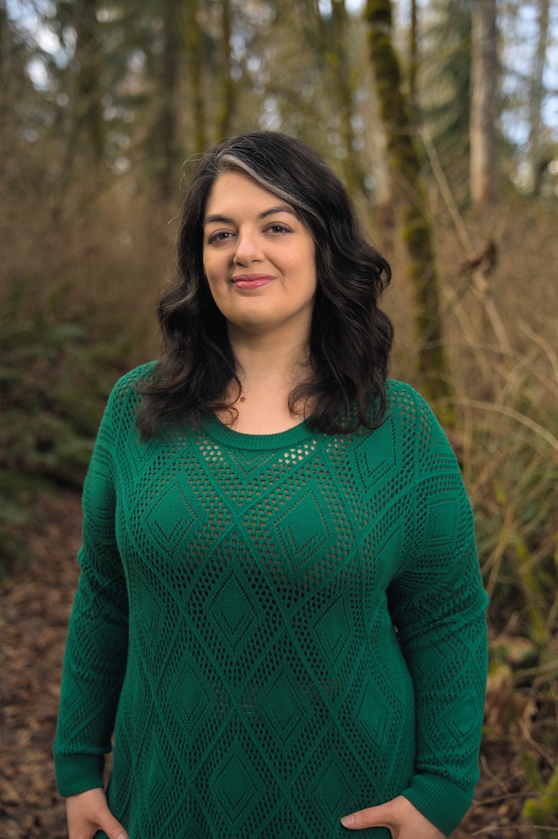 Waist up photo of E.V. Caldwell, fantasy author, standing in a lush forest and greenery.