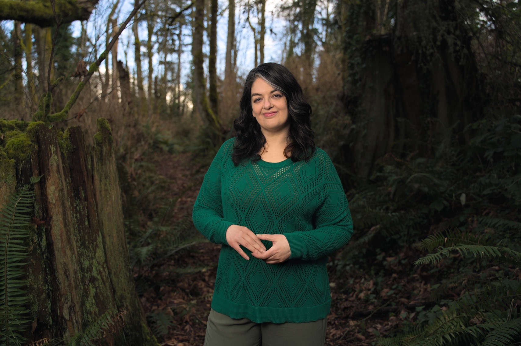 E.V. Caldwell fantasy author standing in forest with dense foliage and leaves.